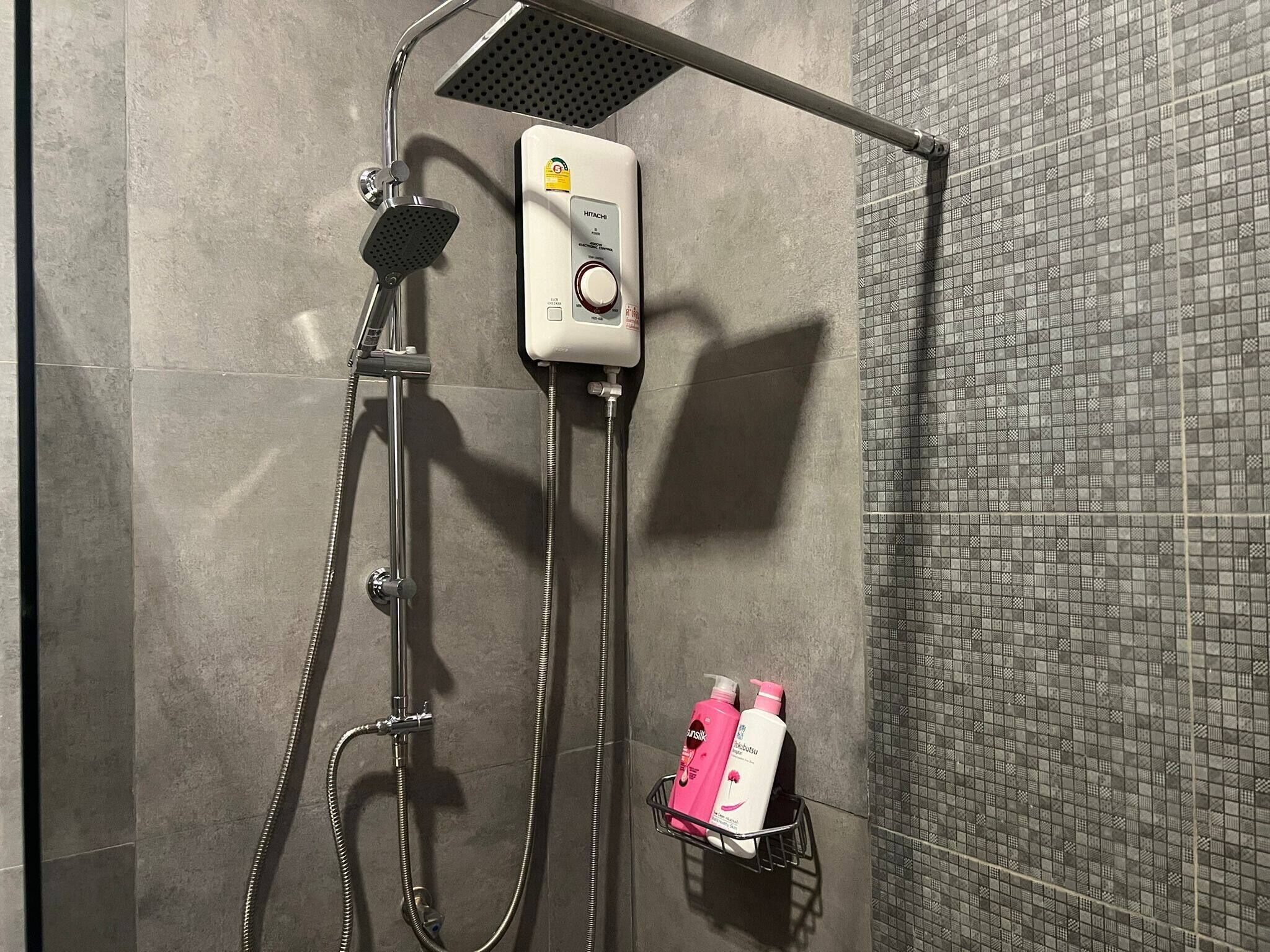 Une douche équipée d’un pommeau de douche à main, d’un panneau de commande mural et d’un porte-savon avec des produits de toilette.