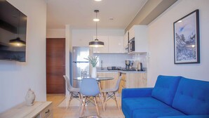 A modern living room with a blue sofa, a dining area with a small table and chairs, and a kitchen with white cabinets and a refrigerator. - w* | Alluring 2BR w/ Balcony in Barranco (Barranco)
