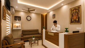 A reception area with a reception desk, a brown sofa, a glass coffee table, and a ceiling fan. - Shri Raghav Palace Hotel Ayodhya (Faizabad)