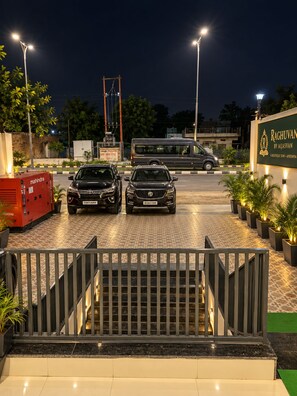 A gated entrance with two cars parked, a bus in the background, and a building with a sign. - Raghuvan by Aijasvan (Faizabad)