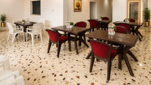A hotel dining area with multiple tables and chairs, a terrazzo floor, and a painting on the wall. - Shri Raghav Palace Hotel Ayodhya (Faizabad)