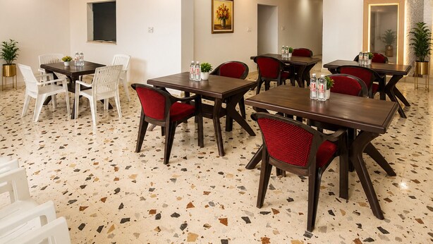 Un comedor de hotel con varias mesas y sillas, piso de terrazo y un cuadro en la pared.