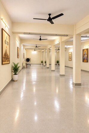 A spacious corridor with ceiling fans, potted plants, and framed artwork on the walls. - Raghuvan by Aijasvan (Faizabad)
