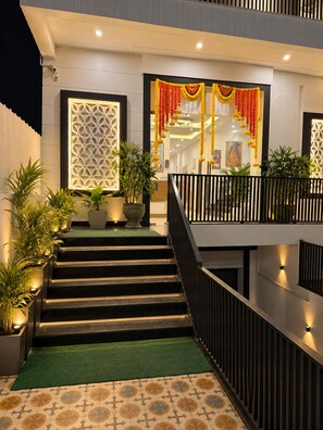 A hotel entrance with a staircase leading to a balcony, decorated with garlands and potted plants. - Raghuvan by Aijasvan (Faizabad)