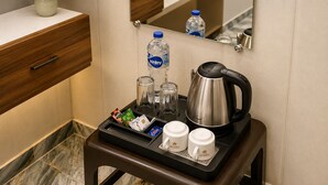 A hotel room with a marble floor, a wooden drawer, a small table with a kettle, cups, a bottle of water, and a tray with snacks. - Shri Raghav Palace Hotel Ayodhya (Faizabad)