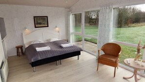 A bedroom with a bed, a chair, a small table, and a window with a view of the outdoors. - Natur Suiten (Outrup)