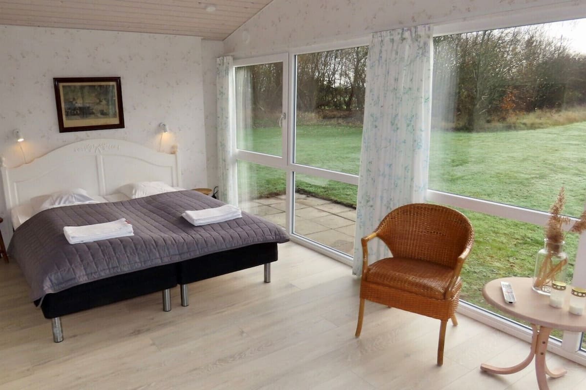 A bedroom with a bed, a chair, a small table, and a window with a view of the outdoors.