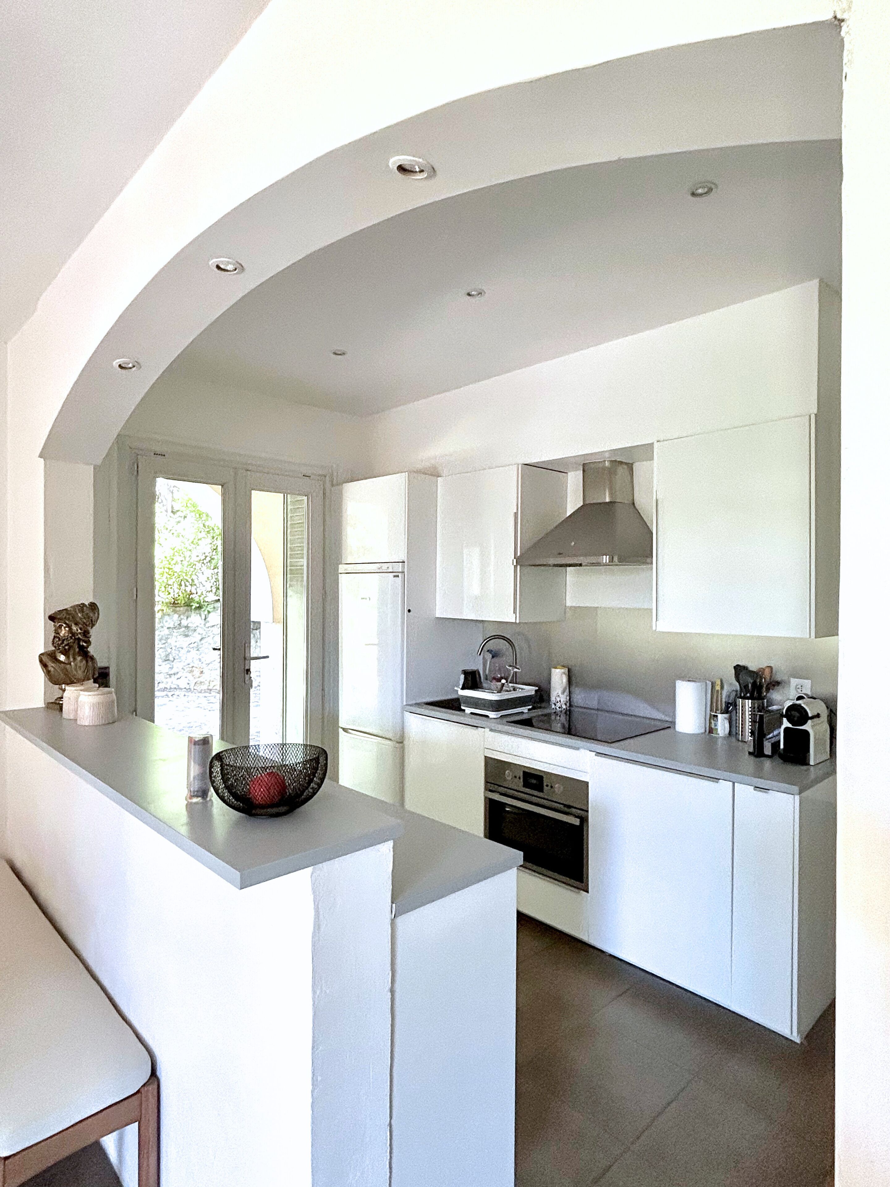 A modern kitchen with white cabinetry, a built-in oven, and a large window providing natural light.