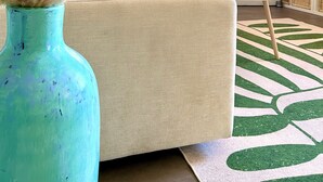 Una sala de estar moderna con un sofá blanco, un tapete verde y blanco estampado y un jarrón azul con plantas secas.