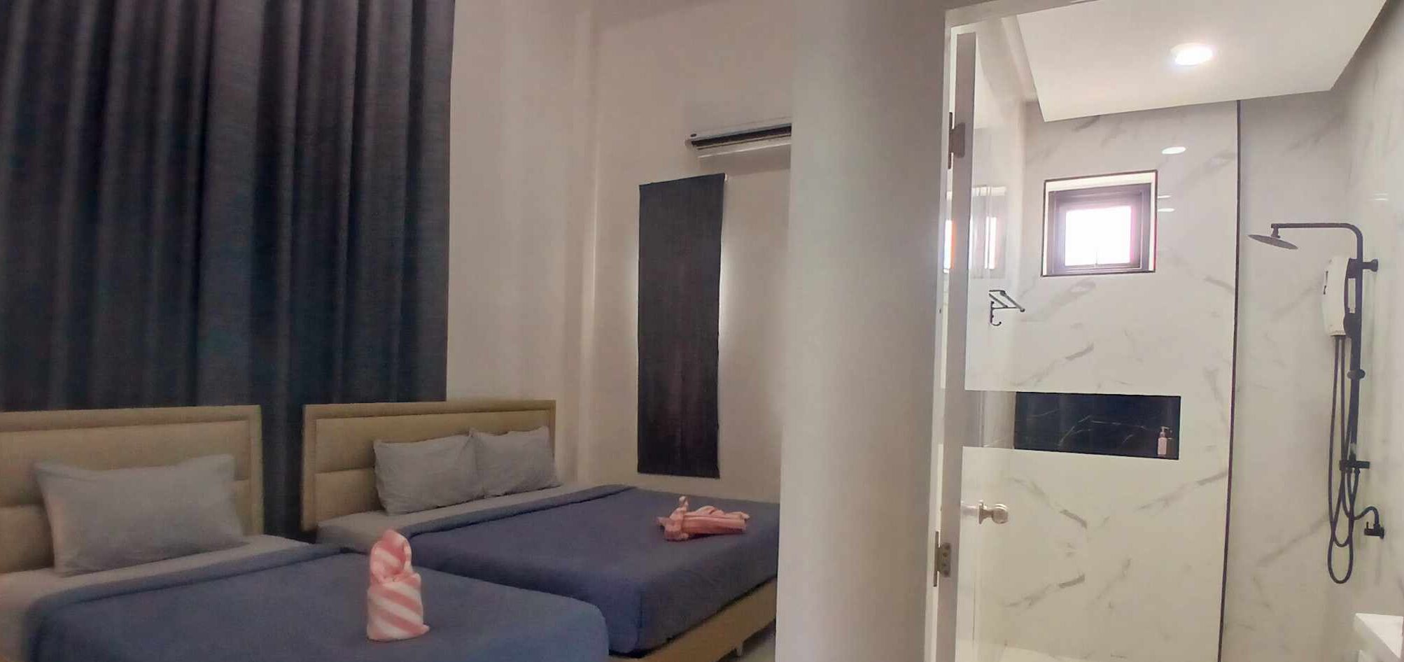 A hotel room with two beds, a shower area, and a window.