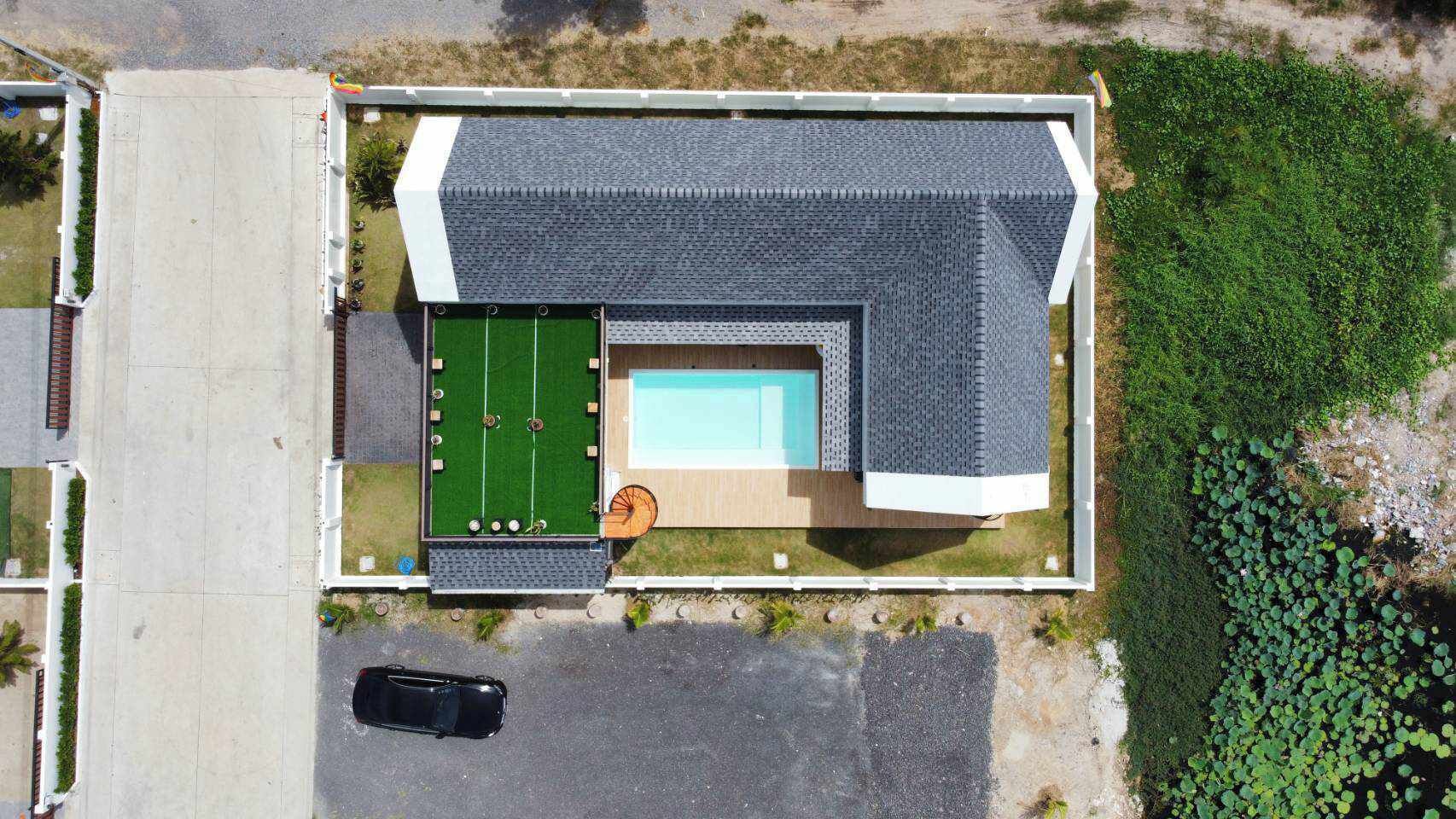 An aerial view of a house with a swimming pool, a tennis court, and a car parked in front.