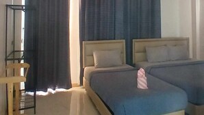 A hotel room with two beds, a standing shelf, and a large window with curtains.