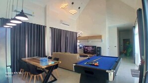 A modern living room with a pool table, a sofa, and a dining area with a table and chairs.