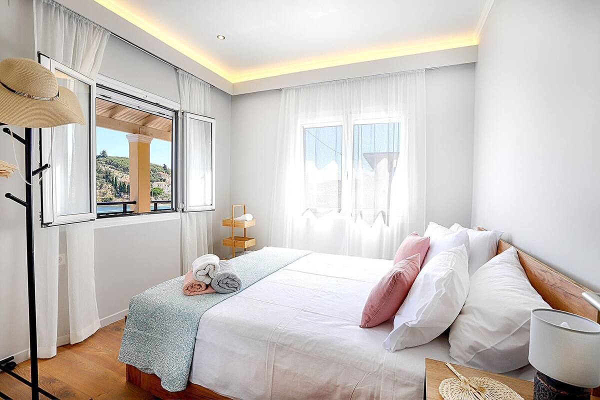 Une chambre d’hôtel avec un lit, une table de chevet, une lampe et une fenêtre donnant sur une colline.