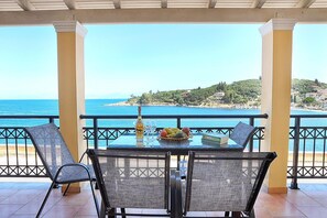 A covered outdoor seating area with a table, chairs, and a view of the sea.