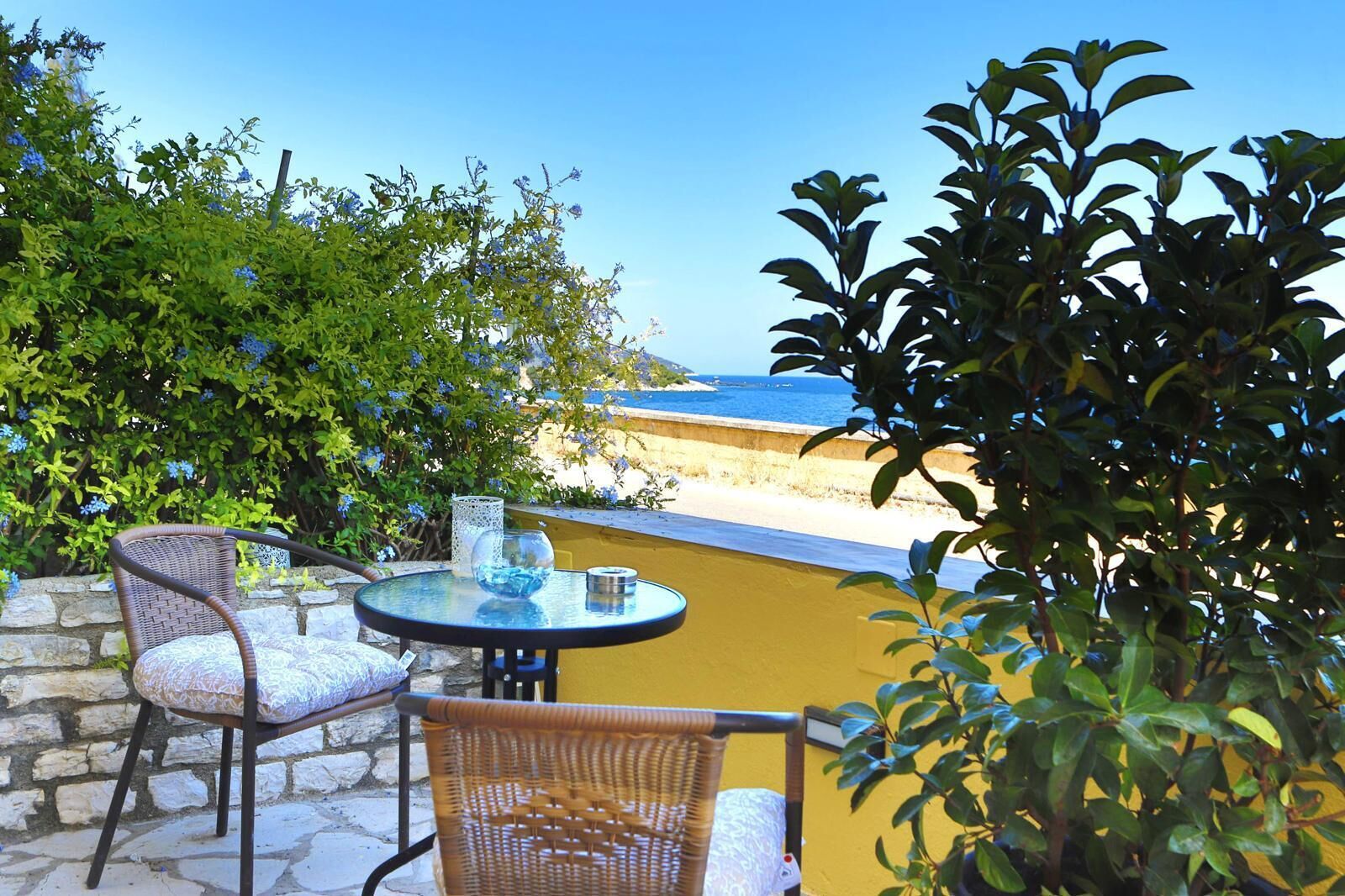 A patio with wicker chairs and a glass table, overlooking a beach.
