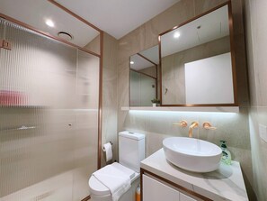 A modern bathroom with a toilet, a sink with a large mirror above it, and a shower enclosure. - Bright & Modern 2BR Apt on Iconic Chapel Street (South Yarra)