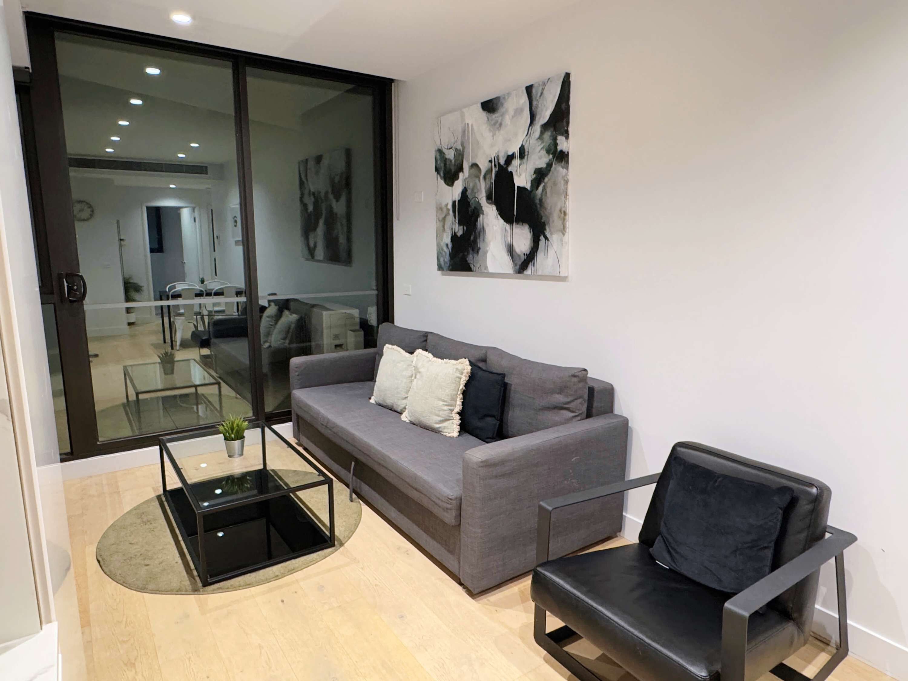 A modern living room with a grey sofa, a black armchair, and a glass coffee table.