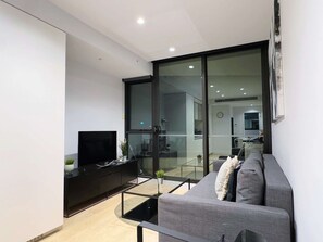 A modern living room with a flat-screen TV, a grey sofa, and a glass coffee table. - Bright & Modern 2BR Apt on Iconic Chapel Street (South Yarra)