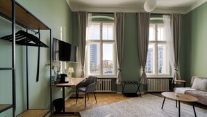 Una habitación moderna con suelo de madera, un escritorio con silla, un sofá, un televisor y un ventanal con cortinas.