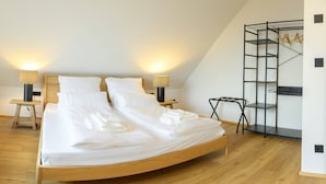 Een slaapkamer met een houten bed, twee bedlampen, een houten nachtkastje, een zwarte metalen open kast en een stoel.