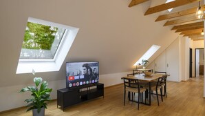 Een moderne woonkamer met een televisie, houten vloeren, een eethoek en een dakraam.