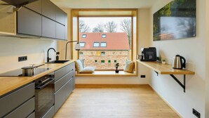 Een moderne keuken met een groot raam, houten vloeren en uitzicht op een bakstenen gebouw.