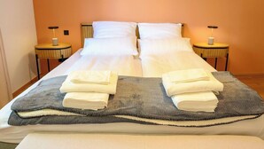 A neatly made bed with white linens and towels, two bedside tables with lamps, and a textured blanket on the bed. - Pausenhof Spreewald - pond view with terrace (Unterspreewald)