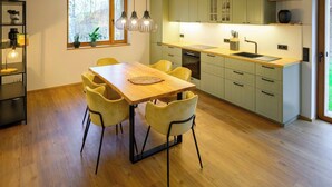 A modern kitchen with a wooden dining table, yellow chairs, and a window with a view of trees. - Pausenhof Spreewald - pond view with terrace (Unterspreewald)
