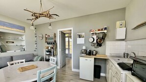 A compact kitchen with a dining area, featuring a white refrigerator, a built-in oven, and a small sink.