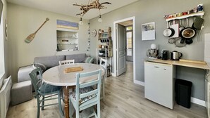 A compact kitchen with a dining area, featuring a wooden ceiling light, a built-in fridge, and a variety of kitchen utensils on the wall.