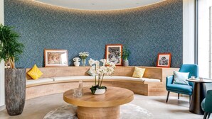 A modern lounge area with a curved seating arrangement, a central wooden coffee table, and a patterned wall. - Zenao Appart'hôtel Saint-Maur-des-Fossés (Saint-Maur-des-Fosses)