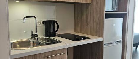 Una cocina moderna con armarios de madera, un lavamanos de acero inoxidable, una cafetera negra y un refrigerador blanco.