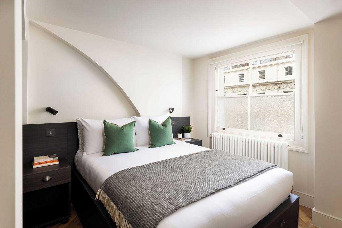 A bedroom with a bed, a nightstand, a window, and a radiator.
