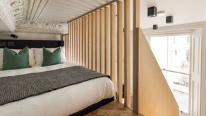 A bedroom with a bed, green pillows, a gray blanket, a wooden slat partition, and a view of the street through a window. - FiveM Notting Hill (London)