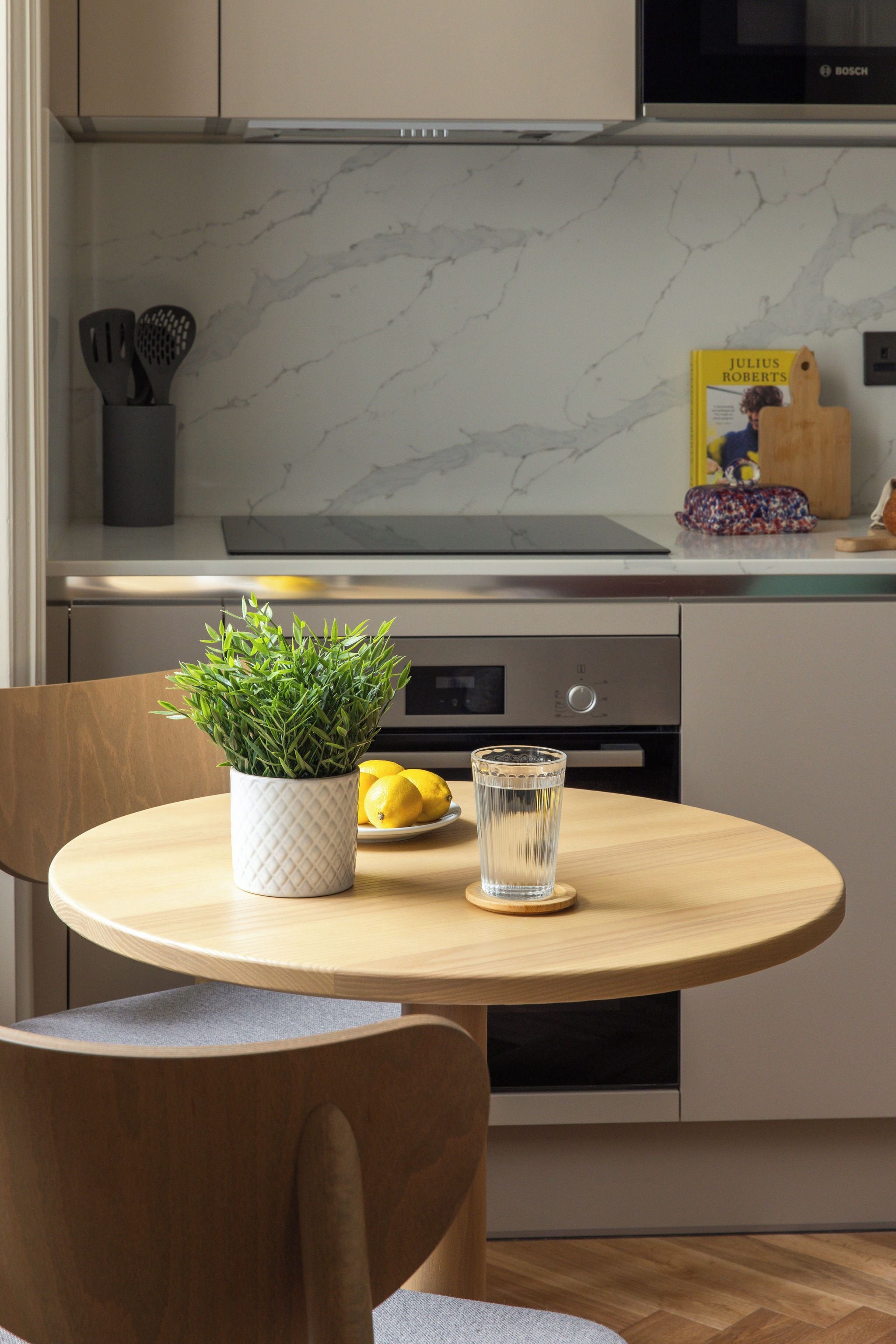 Une cuisine moderne avec une table ronde en bois, une plante en pot et un verre d’eau.