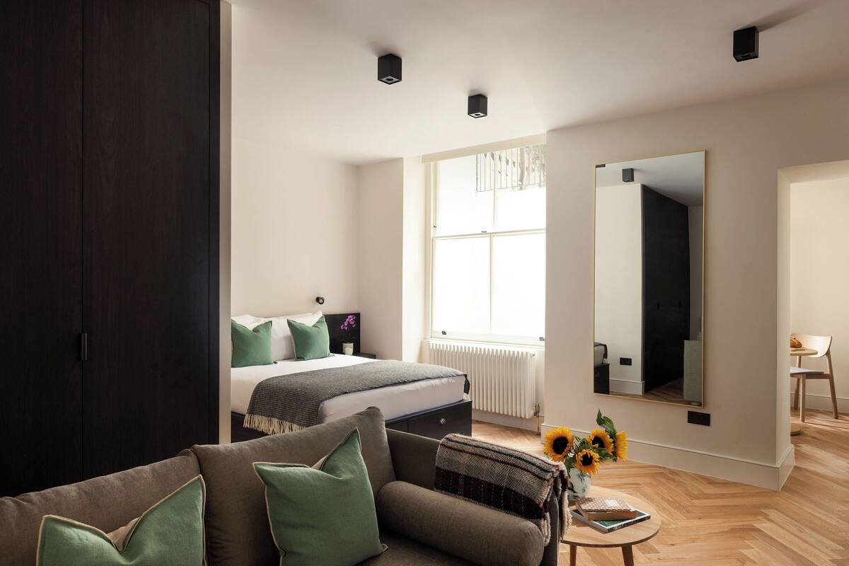 A modern bedroom with a large bed, a sofa, a mirror, and a window.