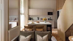A modern kitchen with white cabinets, a central island, and a dining area with two chairs. - FiveM Notting Hill (London)