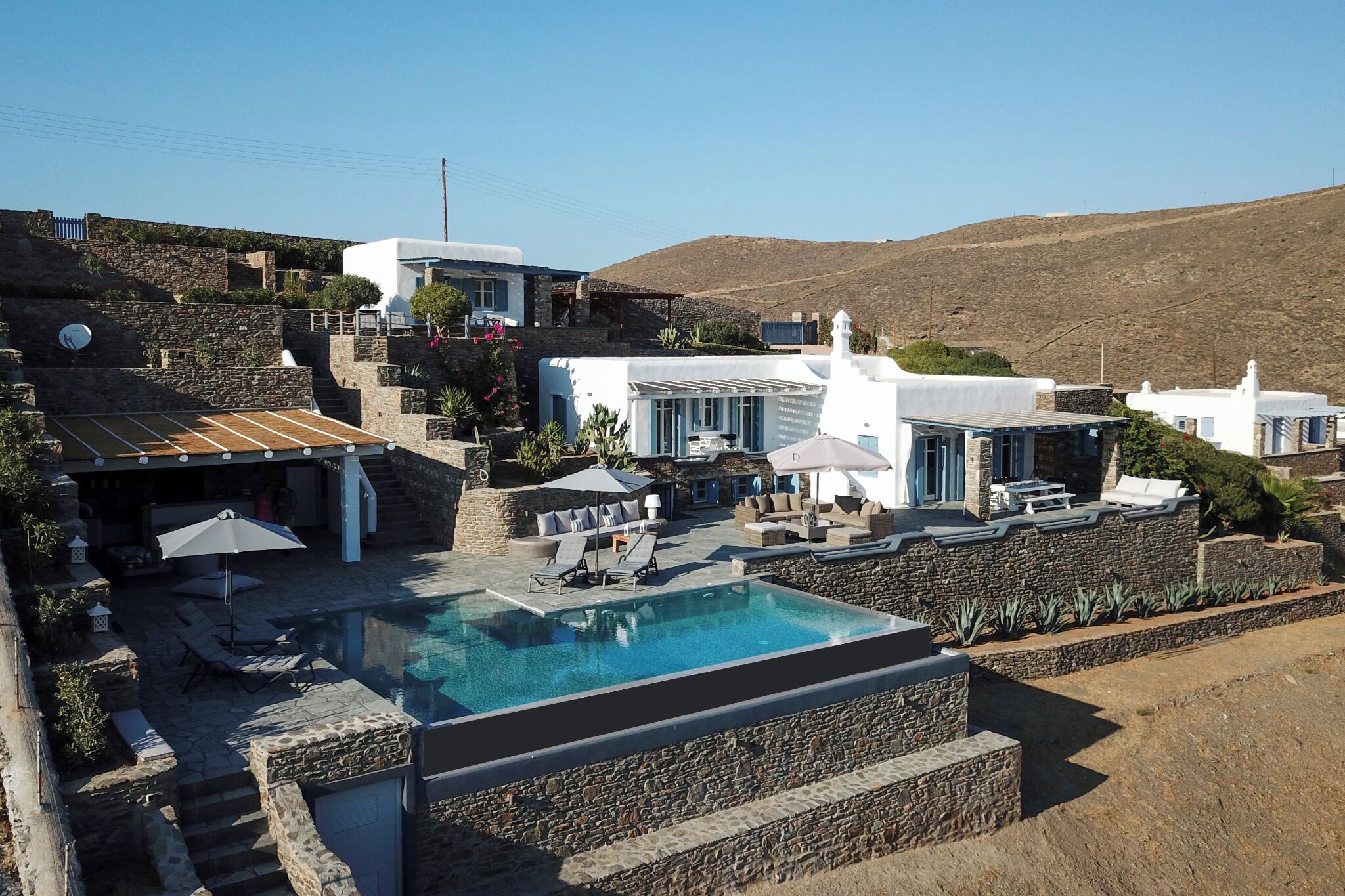 Una villa moderna con piscina, muri in pietra e vista panoramica sulla collina.