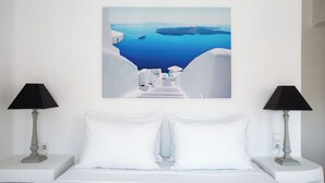 Habitación de hotel con una cama, almohadas blancas, dos mesitas de noche con lámparas y un cuadro con una escena costera.
