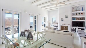 Un interior luminoso y blanco con una mesa de comedor de vidrio, sillas blancas, un sofá y un televisor.