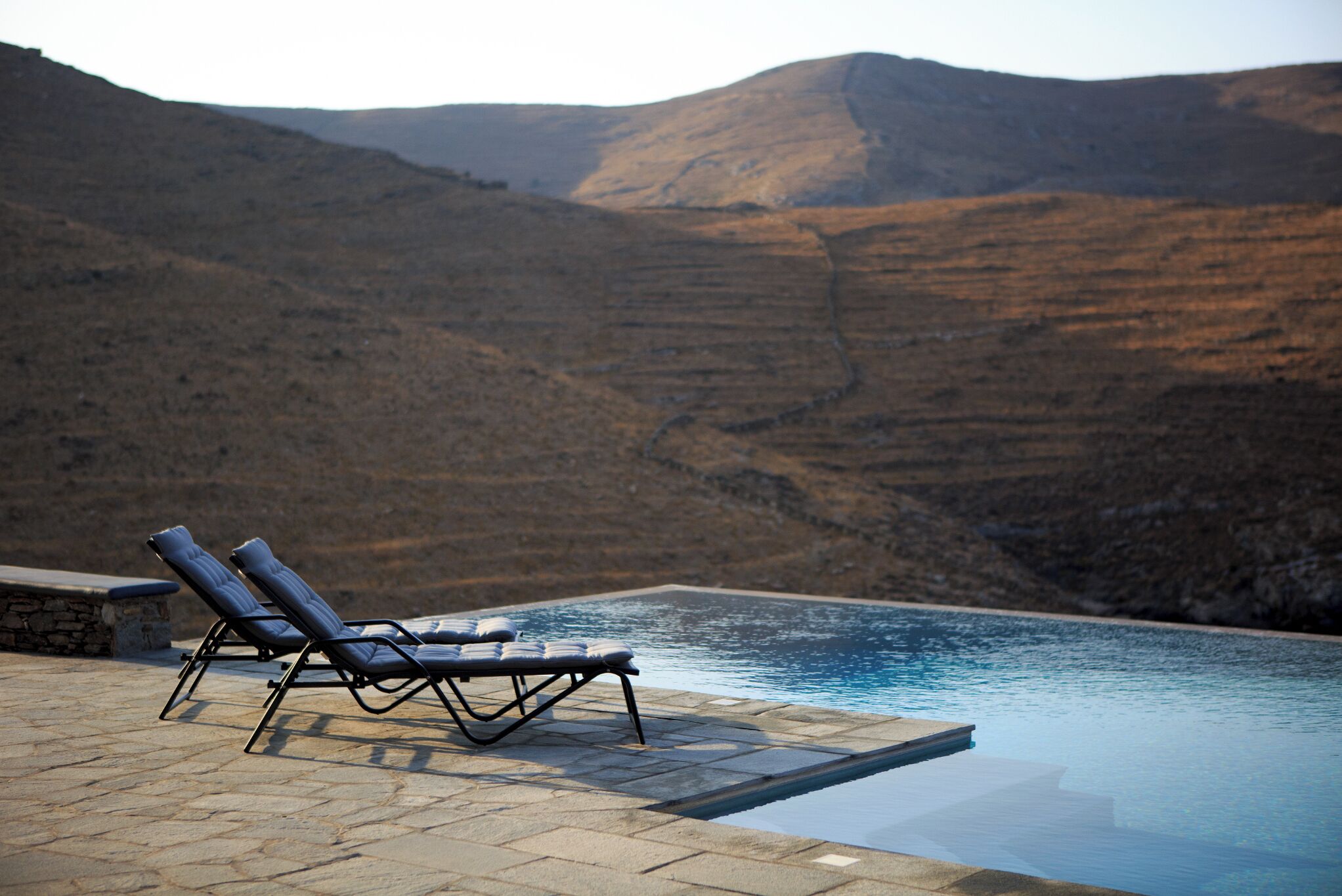 Un espace aménagé au bord de la piscine, avec des chaises longues et une vue sur un paysage montagneux.