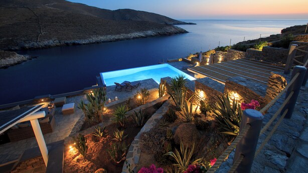 Zona de piscina con vistas al mar, rodeada de escalones de piedra y plantas.