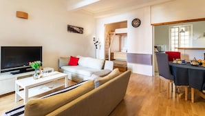 A modern living room with a flat-screen TV, a sofa, a dining table with chairs, and a staircase leading to an upper floor. - ESCALINADA II AP4433  by Riviera Holiday Homes (Villefranche-sur-Mer)