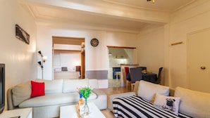 A living room with a sofa, a striped sofa, a coffee table with a vase, and a TV. There is a dining area with a table and chairs in the background. - ESCALINADA II AP4433  by Riviera Holiday Homes (Villefranche-sur-Mer)