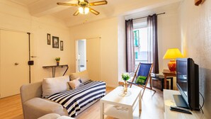 A modern living room with a sofa, a coffee table, a TV, and a ceiling fan. - ESCALINADA II AP4433  by Riviera Holiday Homes (Villefranche-sur-Mer)