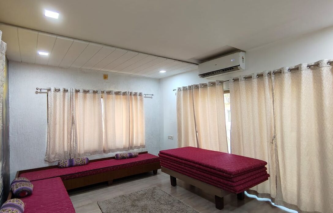 A room with two beds, a bench, and an air conditioning unit.