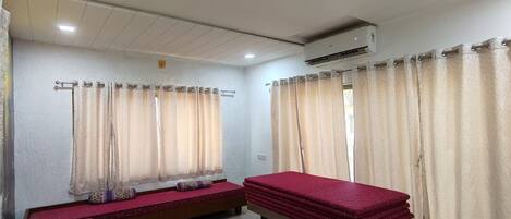 A room with two beds, a bench, and an air conditioning unit.