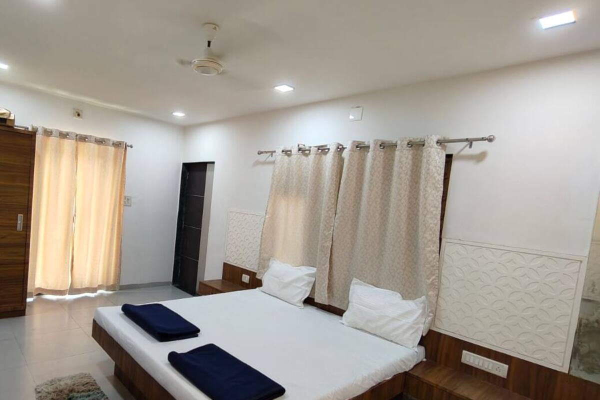A hotel room with a bed, curtains, a ceiling fan, and a light fixture.