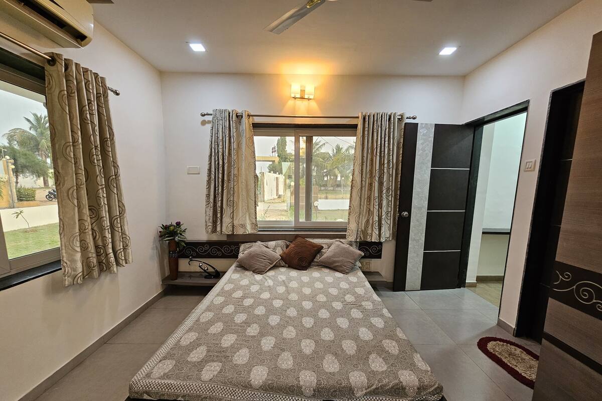 A bedroom with a large bed, curtains, a window with a view, and a door.